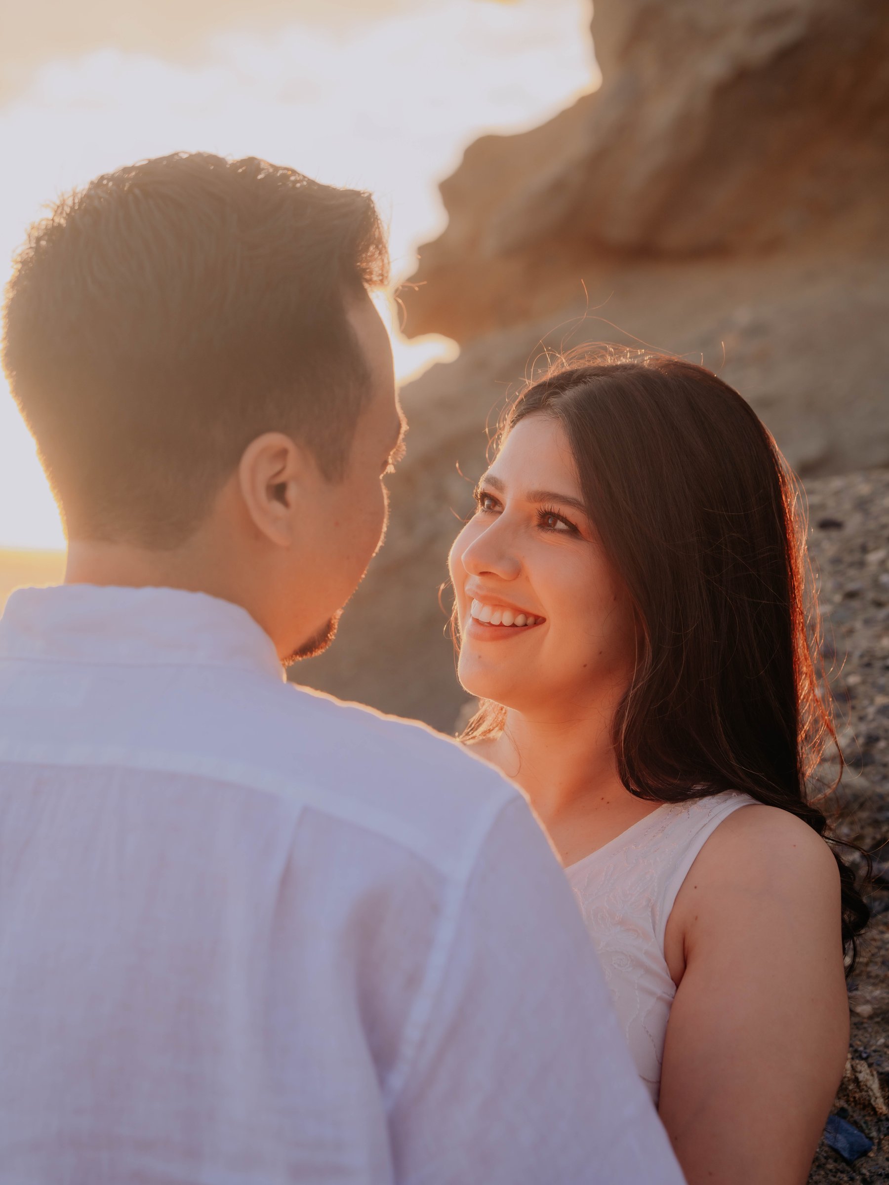Guadalupe and Harrison smiling at each other on a rocky beach at sunset