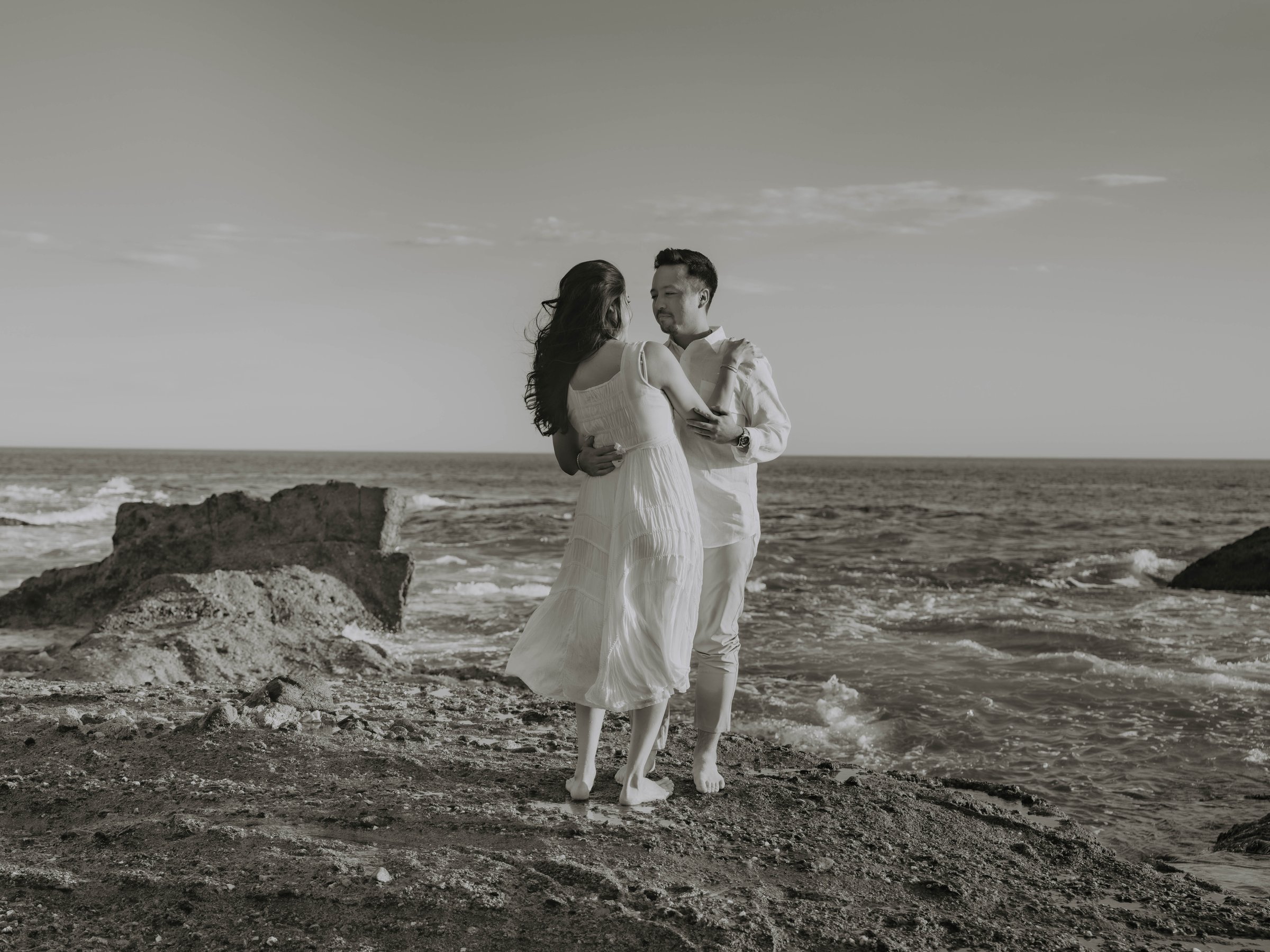 Guadalupe and Harrison embracing on a rocky shoreline, black and white