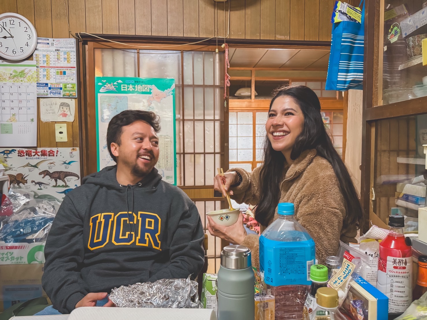 Guadalupe and Harrison laughing together in a kitchen in Japan, sharing a bowl of food